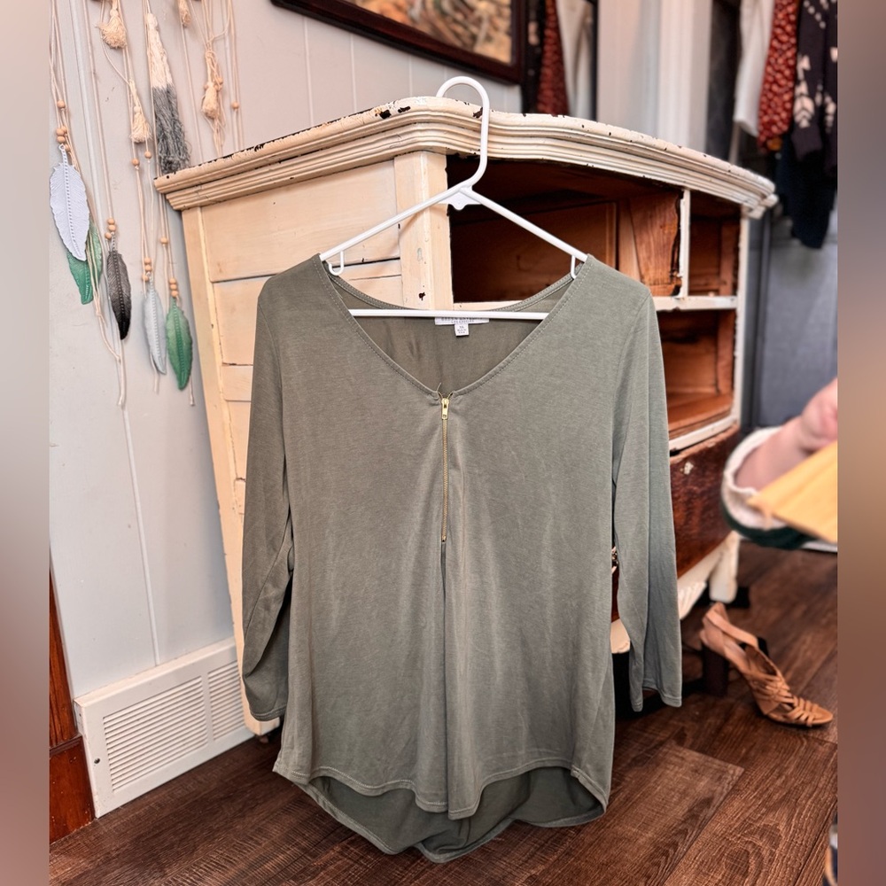 olive green long-sleeve top with a gold zipper detail at the neckline